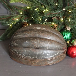 May include: A vintage, gray metal, fluted mold for baking a loaf of bread. The mold is sitting on a gray surface with Christmas ornaments nearby.