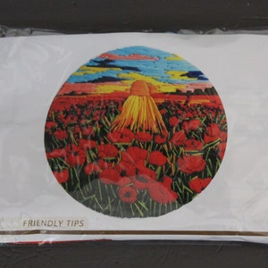 May include: A close-up of a circular embroidery kit featuring a field of red poppies with a yellow sun setting in the background. The kit includes a pre-printed canvas, embroidery floss, and a needle.