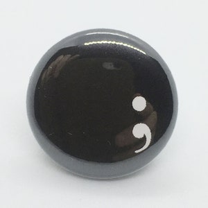May include: A black button with a white semicolon symbol.