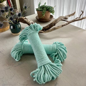 May include: Two spools of light blue cotton rope, each wound into a tight coil. The rope is soft and textured, and the coils are arranged in a criss-cross pattern.
