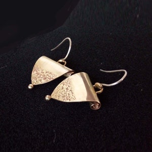 May include: A pair of gold-toned earrings with a triangular shape and a delicate floral pattern. The earrings have a simple hook closure.