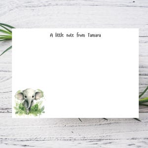 May include: White stationery featuring a watercolour illustration of a baby elephant amidst green foliage. The text "A little note from Tamara" is printed at the top. The stationery is set against a white wood background with green plant accents.