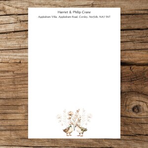 May include: A white card with the text "Harriet & Philip Crane" and "Appledram Villa. Appledram Road, Corsley, Norfolk, NA3 5NT". The card features a watercolour illustration of two ducks facing each other with a floral design behind them.