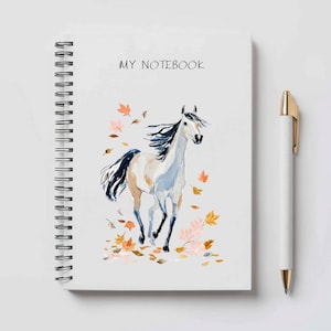 May include: White spiral-bound notebook featuring a watercolour illustration of a running horse and autumn leaves. The text "MY NOTEBOOK" is above the horse. A white pen with a gold clip is beside the notebook.
