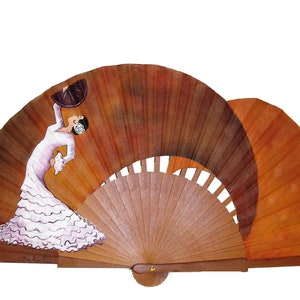 Op de afbeelding: Een handgeschilderde houten waaier met een bruine en oranje achtergrond. De waaier heeft een schilderij van een flamenco-danseres in een witte jurk met roze ruches.