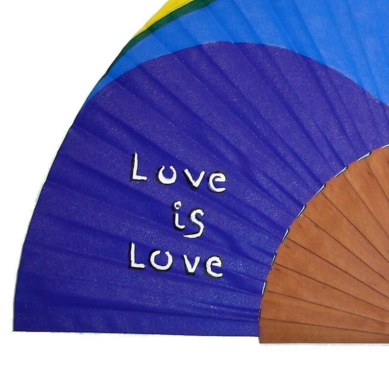 May include: A purple hand fan with a wooden handle. The fan is decorated with a rainbow design and the words "Love is Love" written in white.