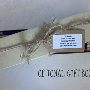 May include: A brown cardboard box tied with twine and a gift tag. The tag has a handwritten message that reads "To Maisie, Good luck on your first day of school Hope to see you soon Love Auntie Claire xxx". The box is labeled "OPTIONAL GIFT BOX".