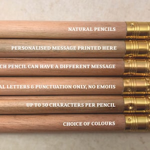 May include: A set of natural wood pencils with gold-colored metal tips and white erasers. Each pencil has a different message printed on it in white letters. The messages are: "NATURAL PENCILS", "PERSONALISED MESSAGE PRINTED HERE", "EACH PENCIL CAN HAVE A DIFFERENT MESSAGE", "CAPITAL LETTERS & PUNCTUATION ONLY, NO EMOJIS", "UP TO 50 CHARACTERS PER PENCIL", and "CHOICE OF COLOURS".
