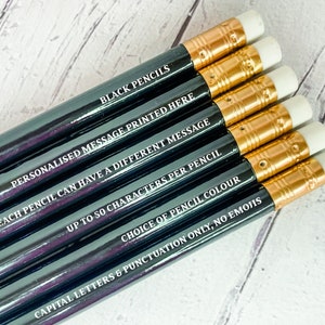 May include: A set of six black pencils with gold accents and white erasers. Each pencil has a different personalized message printed on it. The text on the pencils reads: "BLACK PENCILS", "PERSONALISED MESSAGE PRINTED HERE", "EACH PENCIL CAN HAVE A DIFFERENT MESSAGE", "UP TO 50 CHARACTERS PER PENCIL", "CHOICE OF PENCIL COLOUR", and "CAPITAL LETTERS & PUNCTUATION ONLY, NO EMOJIS".