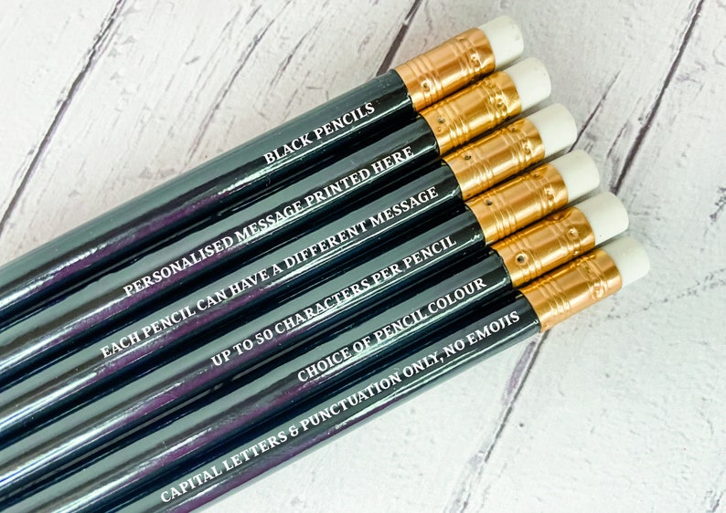 May include: A set of six black pencils with gold accents and white erasers. Each pencil has a different personalized message printed on it. The text on the pencils reads: "BLACK PENCILS", "PERSONALISED MESSAGE PRINTED HERE", "EACH PENCIL CAN HAVE A DIFFERENT MESSAGE", "UP TO 50 CHARACTERS PER PENCIL", "CHOICE OF PENCIL COLOUR", and "CAPITAL LETTERS & PUNCTUATION ONLY, NO EMOJIS".