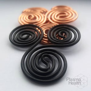 Op de afbeelding: Een close-up van een driedimensionaal draadbeeld met drie zwarte spiralen en drie koperen spiralen. Het beeld staat op een wit oppervlak.