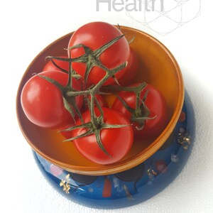 May include: A bowl of red tomatoes on a blue and gold patterned base. The tomatoes are on a vine and are arranged in a bowl.