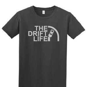 May include: A dark gray t-shirt with a white graphic design that says "The Drift Life" with a car drifting around a corner.