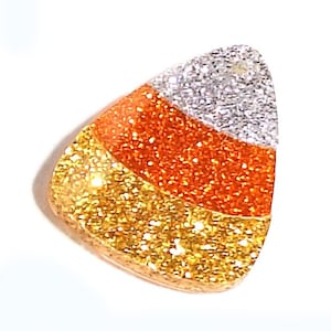 May include: A triangular candy corn shaped charm featuring three horizontal bands of glittery texture. The top section is silver, the middle section is bright orange, and the bottom section is a vibrant yellow, all with a reflective finish.