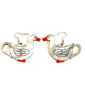 May include: A pair of whimsical duck-shaped earrings. The earrings feature a pearlescent white body with black outline details, red beaks and feet, and silver-tone ear wires. The earrings are a fun accessory.
