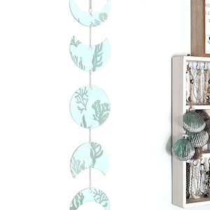 May include: A light blue moon phase wall hanging with a sea life design. Each moon phase is decorated with a green seaweed pattern.