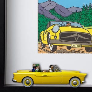 Puede incluir: Una imagen enmarcada que presenta un coche descapotable amarillo con pasajeros y un coche de juguete a juego debajo. La obra de arte representa un paisaje monta&ntilde;oso y un coche de dibujos animados con la matr&iacute;cula "20510-209".