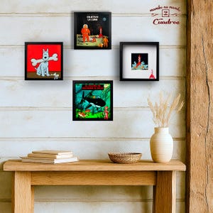 May include: Four square black-framed wall art pieces featuring Tintin-themed illustrations. One shows a white dog with a bone, another a space scene with the text "OBJETIVO LA LUNA", one a rocket, and the last an underwater scene with "EL TESORO DE RACKHAM EL ROJO".