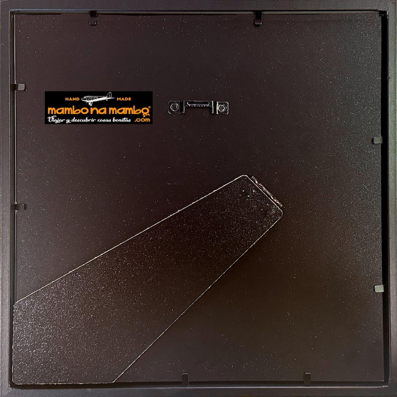 May include: The back of a black picture frame with a built-in easel and hanging hardware. A sticker in the upper left corner reads "Hand Made mambo na mambo Viajar y descubrir cosas bonitas .com".