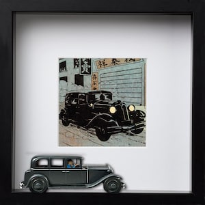 May include: A framed artwork featuring a black vintage car illustration in a Japanese style. Below the artwork is a miniature model of a black car with a driver. The artwork is in a black frame.