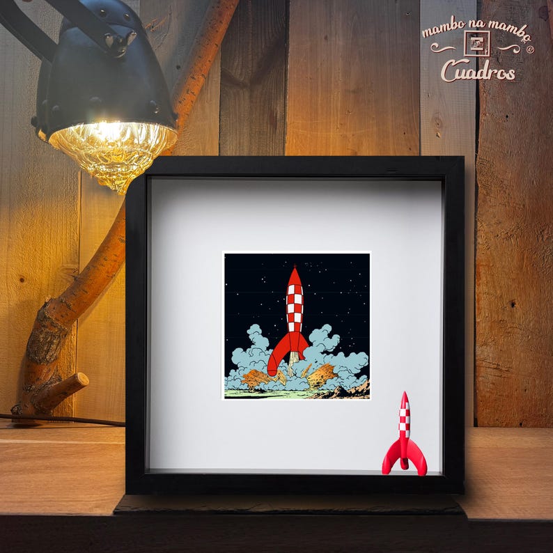 May include: A square black frame containing a print of a red and white chequered rocket ship launching into a dark starry sky with clouds of smoke. A small three-dimensional red and white chequered rocket figurine is attached to the bottom right.