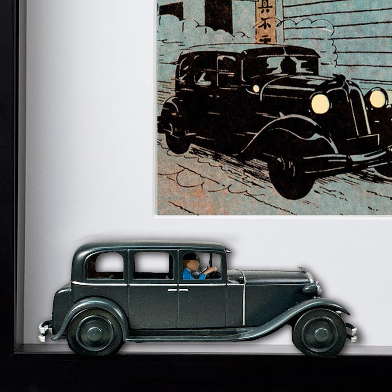 May include: A framed image featuring a vintage black car model and a comic strip illustration of a similar car. The model car is dark green with a driver figure. The comic strip shows a black car on a snowy street.
