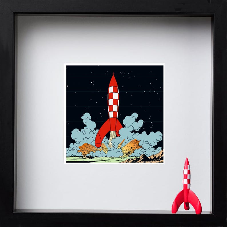 May include: A framed square print featuring a red and white chequered rocket ship launching into a dark starry sky with clouds of smoke and fire at the base. A small, three-dimensional red and white chequered rocket figurine stands in the corner.