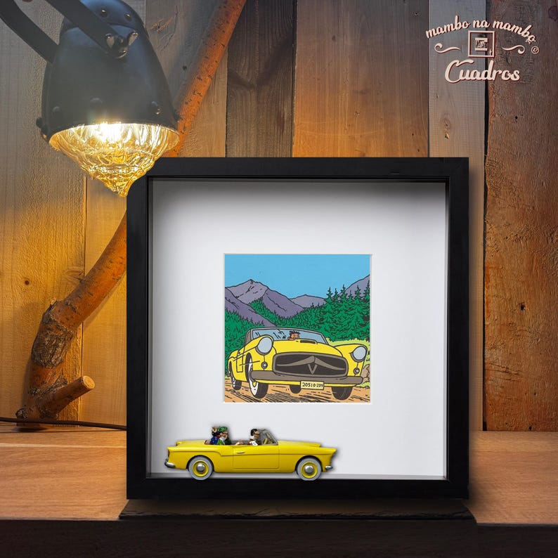 Puede incluir: Una impresi&oacute;n enmarcada de un coche descapotable amarillo con un fondo de monta&ntilde;a. Un coche amarillo en miniatura con dos figuras se encuentra frente a la impresi&oacute;n enmarcada. El marco es negro y el fondo es de madera.