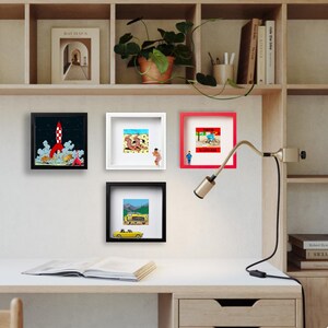 Puede incluir: Una colecci&oacute;n de obras de arte enmarcadas, cada una con una ilustraci&oacute;n &uacute;nica. Los marcos son negros, blancos y rojos, y el arte representa escenas como un lanzamiento de cohete, ba&ntilde;istas, un ciclista y un descapotable amarillo. El arte se exhibe en un escritorio blanco.
