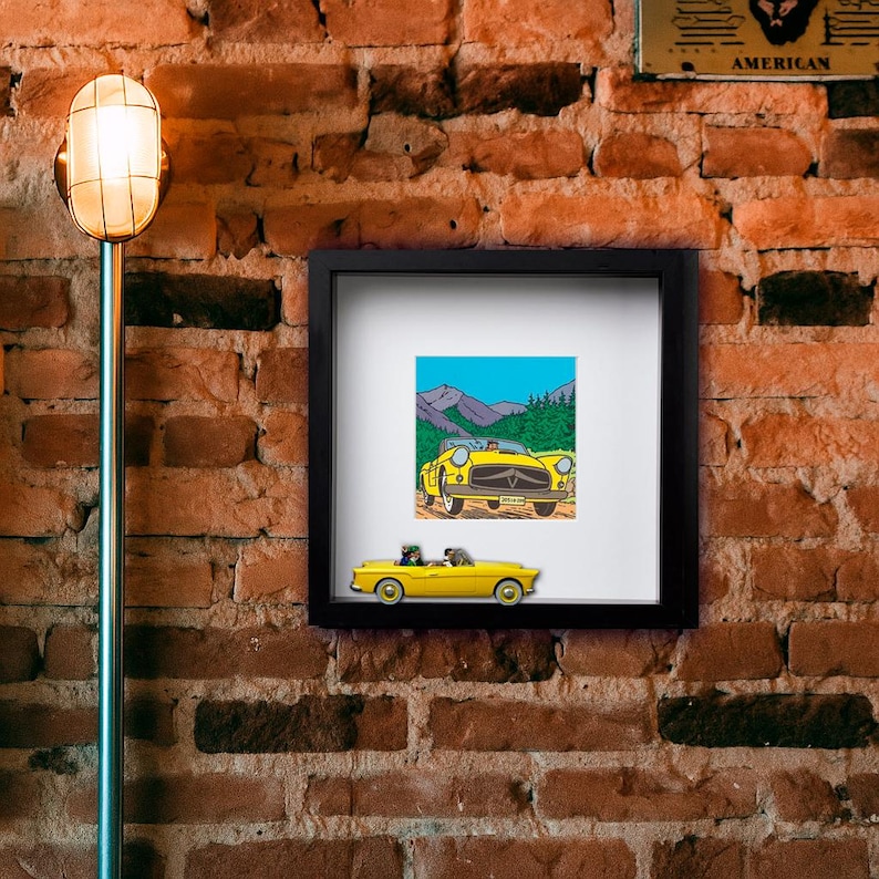 Puede incluir: Una impresi&oacute;n enmarcada y un modelo en miniatura de un coche descapotable amarillo. La impresi&oacute;n presenta una ilustraci&oacute;n de dibujos animados de un coche amarillo con un fondo de monta&ntilde;a. El coche modelo tambi&eacute;n es amarillo.