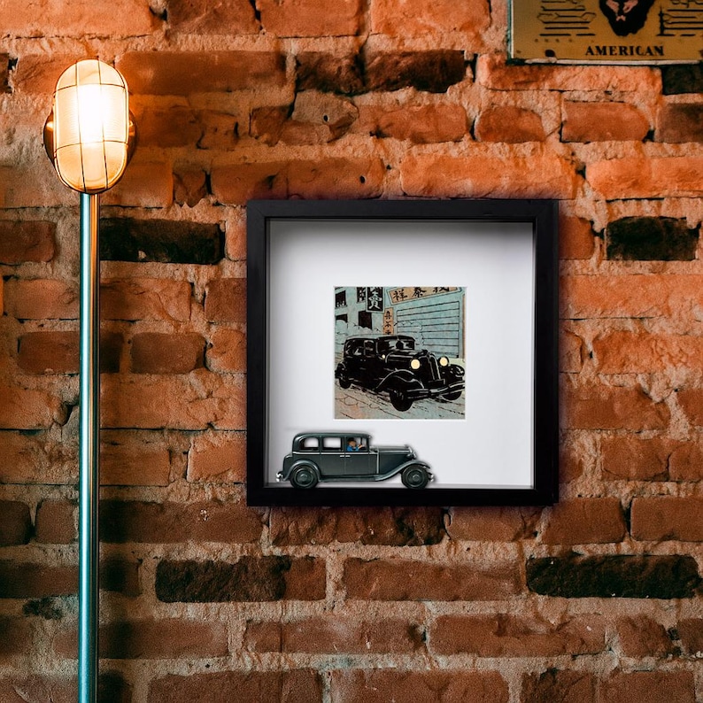 May include: A black framed print of a vintage car with Japanese text, mounted on a brick wall. Below the print is a small, dark gray model car. A vintage-style lamp is on the left.