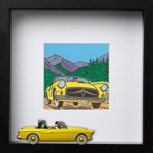 Puede incluir: Una impresi&oacute;n enmarcada y un coche de juguete de un descapotable amarillo. La impresi&oacute;n representa un descapotable amarillo conduciendo por un camino de tierra con monta&ntilde;as y &aacute;rboles al fondo. El coche de juguete es una versi&oacute;n en miniatura del coche de la impresi&oacute;n.