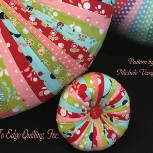 May include: Two round, colorful fabric pincushions. The larger pincushion is heart-shaped and the smaller pincushion is round. Both pincushions are made of a variety of fabrics with floral and polka dot patterns. The pincushions are on a black surface. Pattern by Michele Vangraan. © Edge To Edge Quilting, Inc.