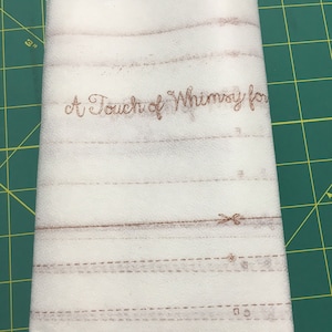 May include: A rectangular sheet of white, semi-transparent foam packaging material featuring brown printed lines and symbols. The text "A Touch of Whimsy for" is printed in a cursive font, accompanied by various dashed lines and small icons.