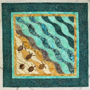 Könnte beinhalten: Ein gesteppter Wandbehang mit einem blaugrünen Rand und einem beige-blauen Innenbereich. Der Innenbereich zeigt ein Muster aus Wellen und Meeresschildkröten.