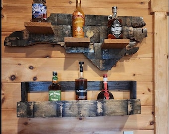 May include: A wooden shelf shaped like the state of North Carolina, with multiple shelves for displaying bottles of liquor. The shelf is made from reclaimed wood and has a rustic, distressed look. The shelf is mounted on a wooden wall.