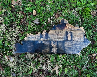 May include: A wooden cutout of the state of Kentucky, made from reclaimed bourbon barrel staves. The wood is dark brown with black char marks and has a rustic, aged appearance.
