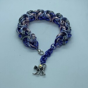 May include: A chainmail bracelet with a monkey charm. The bracelet is made of interwoven metal rings in shades of blue, silver, and pink. The monkey charm is silver-colored with a crystal accent. The bracelet has a lobster clasp closure.