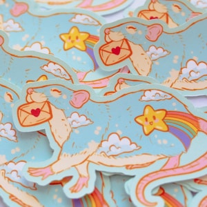 May include: A stack of colorful stickers featuring a cartoon rat holding a letter with a heart on it. The rat is flying through the clouds with a rainbow and a star behind it.