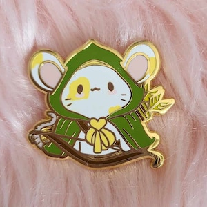 May include: A gold-colored enamel pin featuring a cartoon mouse wearing a green hooded cloak and holding a bow and arrow. The mouse has yellow and white fur and a heart-shaped bow.