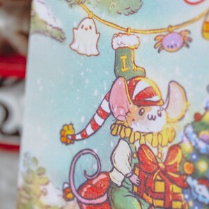 May include: A cartoon mouse wearing a red and white striped hat and a green and yellow outfit holds a red and yellow gift box. The mouse is standing in front of a decorated Christmas tree with ornaments and lights. The background is a light blue with snowflakes.