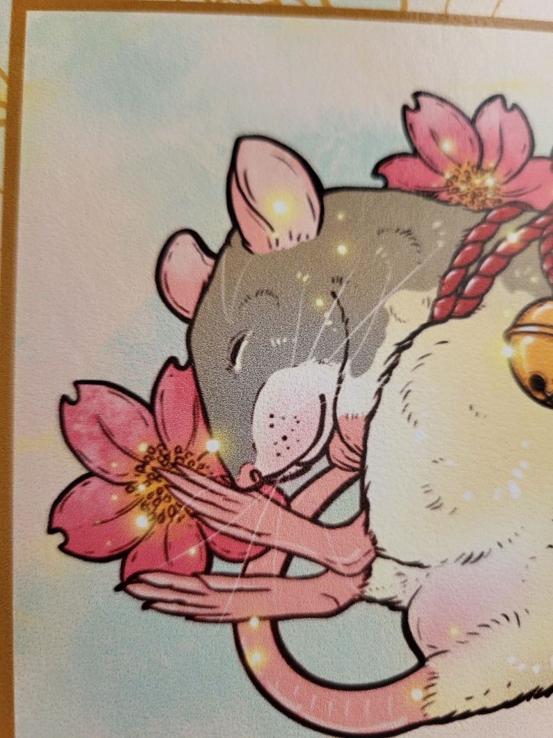 May include: Illustration of a rat with gray fur, pink ears, and a pink nose, surrounded by pink cherry blossoms. The rat has a red rope and a gold bell. The background is a soft, light blue and yellow.