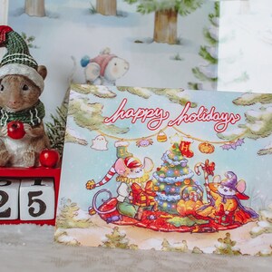 May include: A Christmas card with a blue background featuring three mice dressed in holiday attire. The mice are gathered around a decorated Christmas tree with presents and candy canes. The card reads "Happy Holidays".