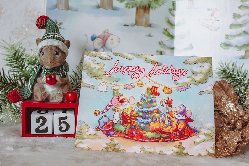 May include: A Christmas card with a blue background featuring three mice dressed in holiday attire. The mice are gathered around a decorated Christmas tree with presents and candy canes. The card reads "Happy Holidays".