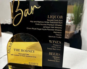 May include: A black acrylic bar menu with gold lettering and accents. The menu lists liquor, wines, and beers, including Bacardi Dark Rum, Jameson Irish Whiskey, and Guinness Stout. A gold-colored section highlights a signature drink, "The Rodney."