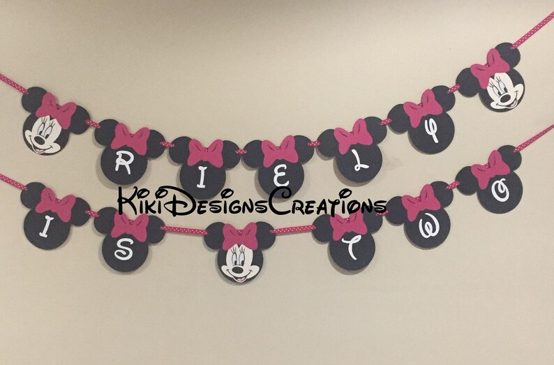 May include: A black and pink Minnie Mouse themed banner with the letters "RILEY IS" in white on black circles. Each circle has a pink bow on top.