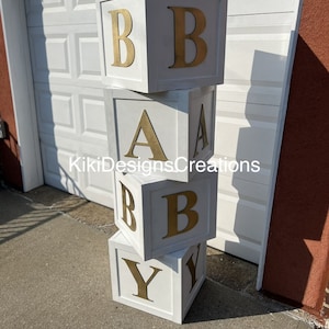 Puede incluir: Bloques de madera blancos apilados para deletrear "BABY" con letras doradas. Los bloques est&aacute;n pintados de blanco y tienen un aspecto ligeramente desgastado.