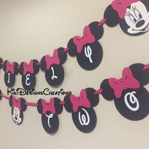 May include: A black and pink Minnie Mouse themed banner with the letters "RILEY" and "OW" in white. The banner is strung together with red and white polka dot ribbon.