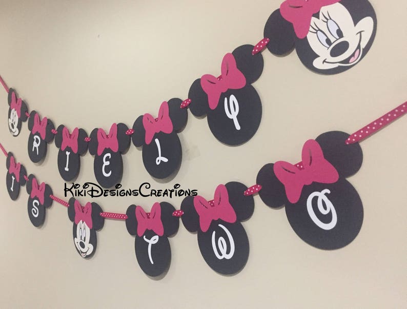 May include: A black and pink Minnie Mouse themed banner with the letters "RILEY" and "OW" in white. The banner is strung together with red and white polka dot ribbon.