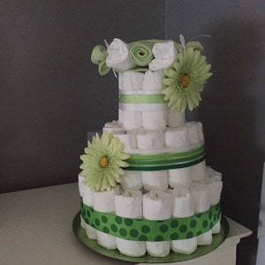 Puede incluir: Un pastel de pa&ntilde;ales de tres niveles decorado con cinta verde y blanca, cinta de lunares verdes y flores verdes. El pastel est&aacute; hecho de pa&ntilde;ales enrollados.